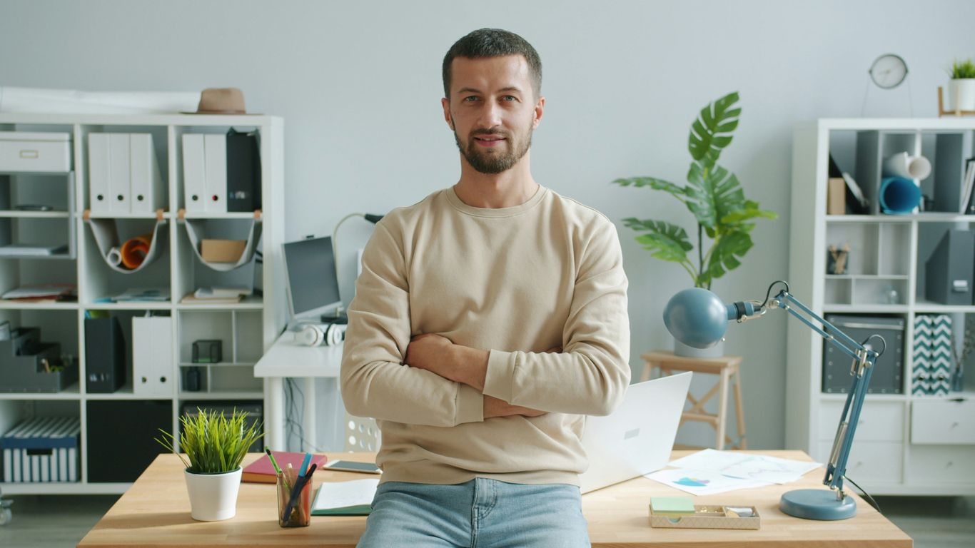 Man with arms crossed in modern office workspace.